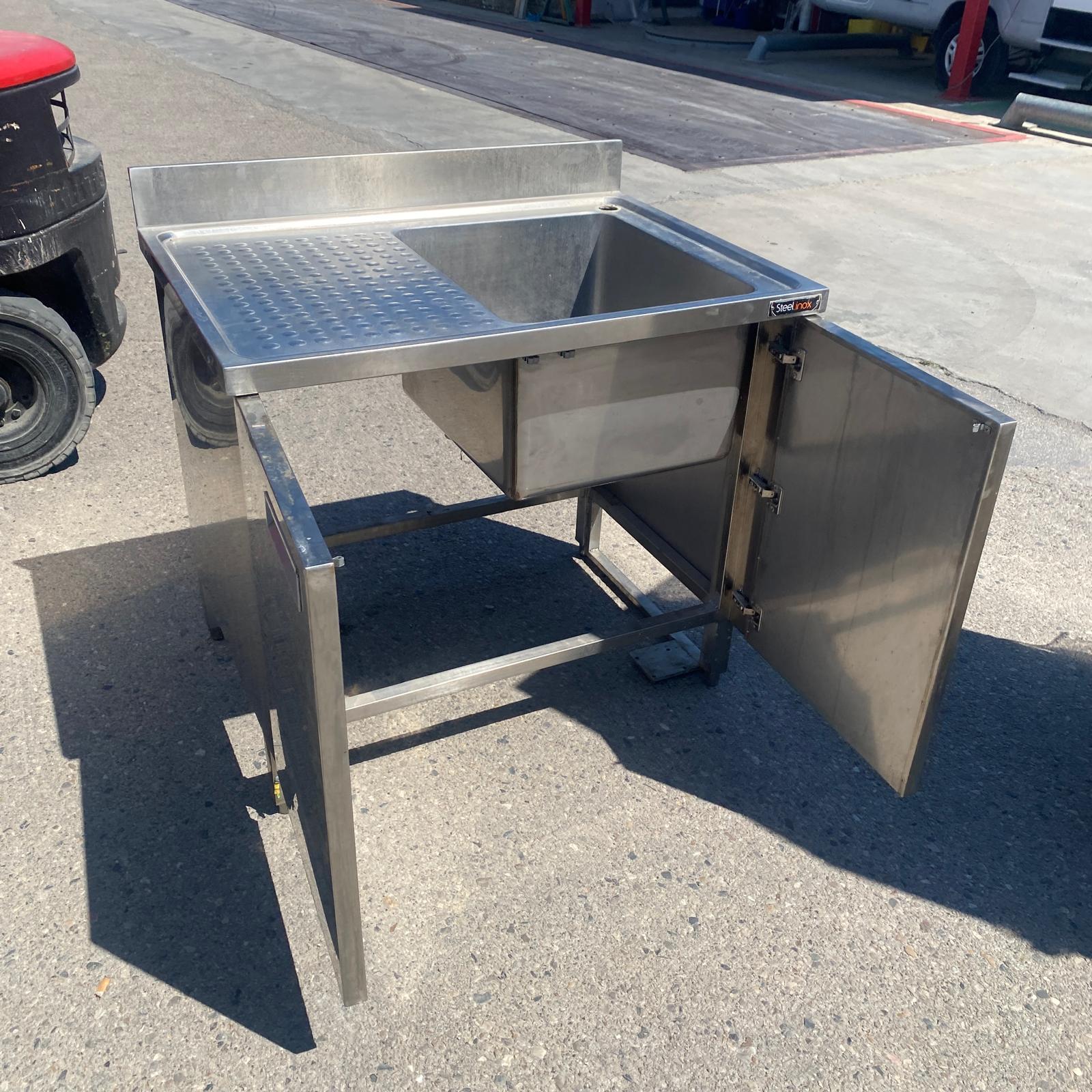 Fregadero industrial Steelinox con armario inferior y puerta lateral abierta para almacenamiento.