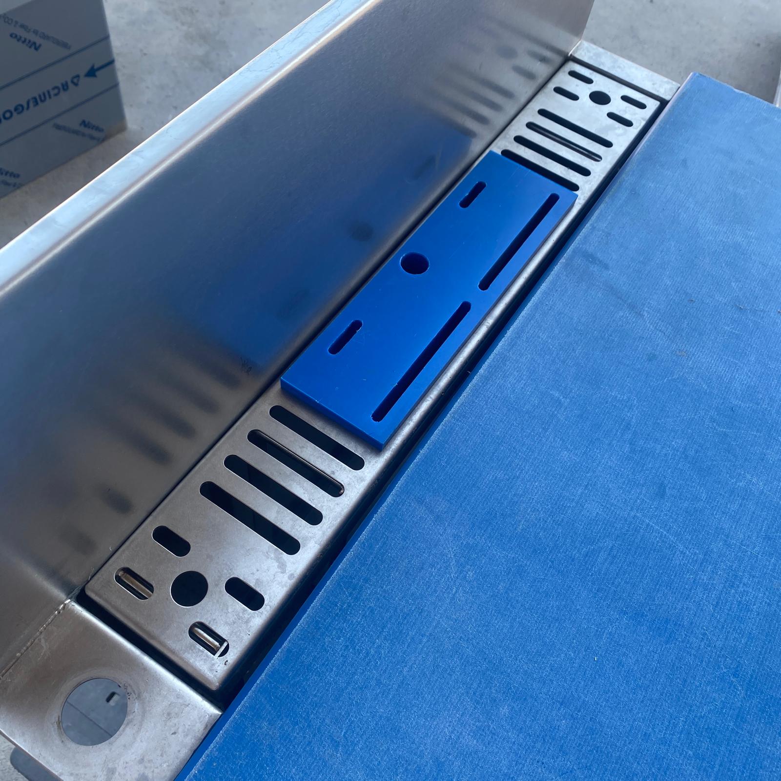 Detalle de mesa de preparación para pescado con tabla azul, escurridor perforado y zona de desagüe.