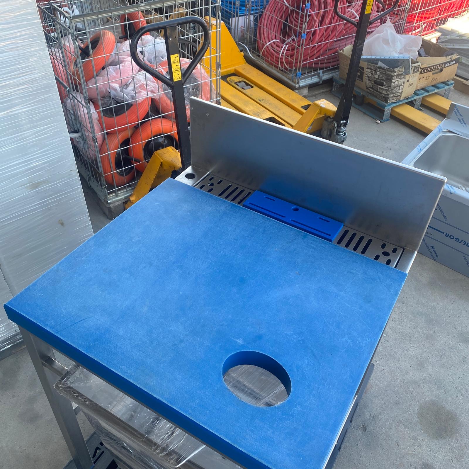 Vista superior de mesa de preparación para pescado con tabla de corte azul y orificio para residuos.