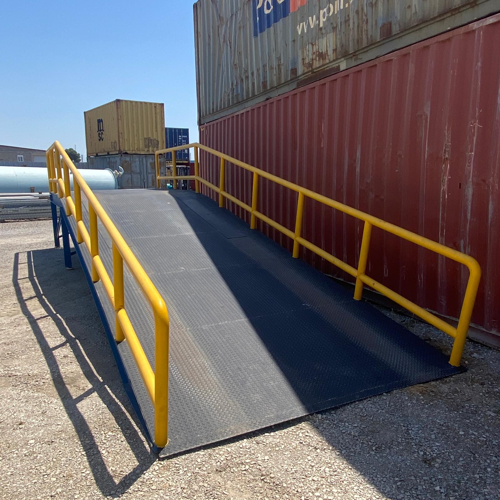 Rampa metálica industrial con plataforma superior y barandillas amarillas de seguridad.
